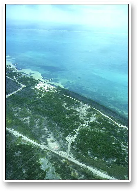 Arial view: the reef side - This picture shows the reef (east) side of Ambergris Caye south of San Pedro. The stretch is typical: beach with a few houses, a road running more or less along the coast, nice flats, deeper parts and in the distance the protective reef visible as a white line just under the horizon.
