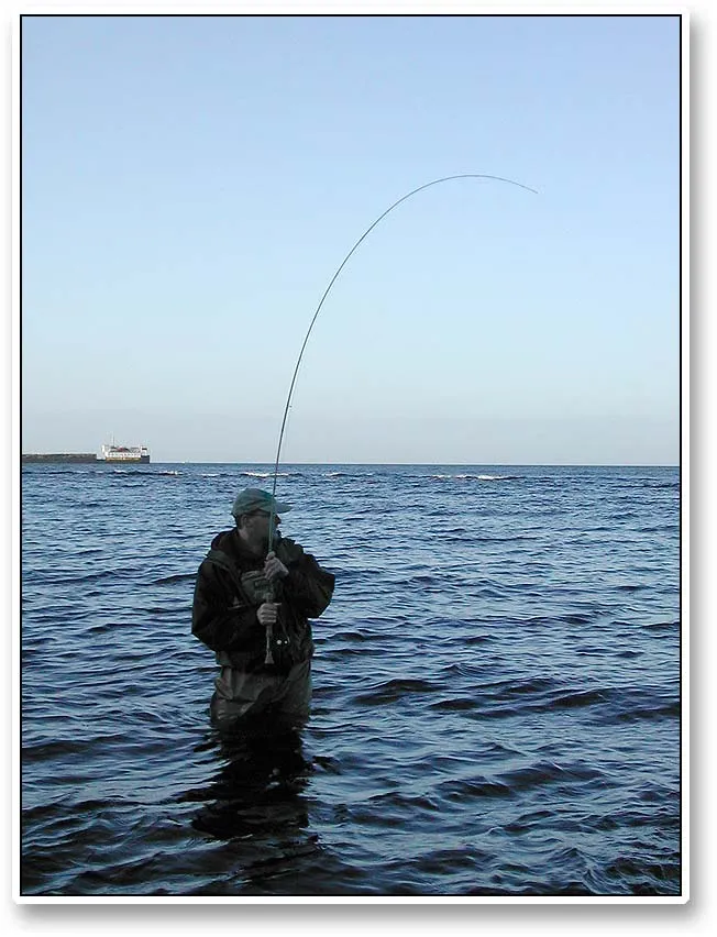 Martin into a fish - Martin has hooked a nice fish in the last daylight on the northern side of Bornholm. In the back a large ship has found shelter from the rough south eastern winds.